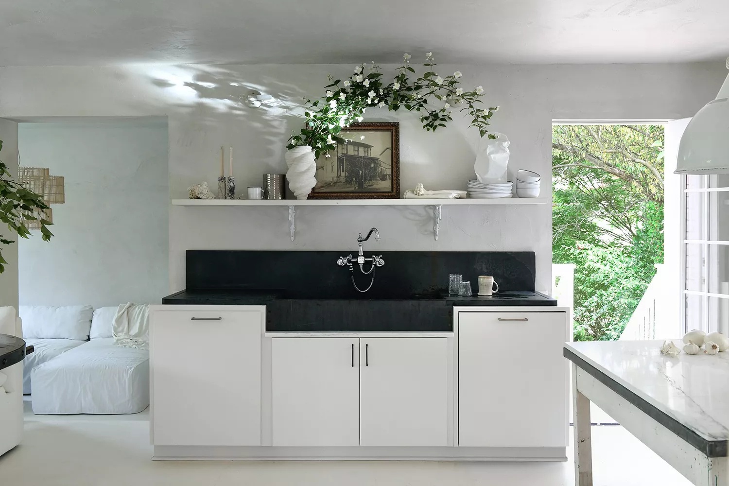 All-white kitchen with black stone backsplash, countertops, and farmhouse sink as a stunning black-and-white focal point
