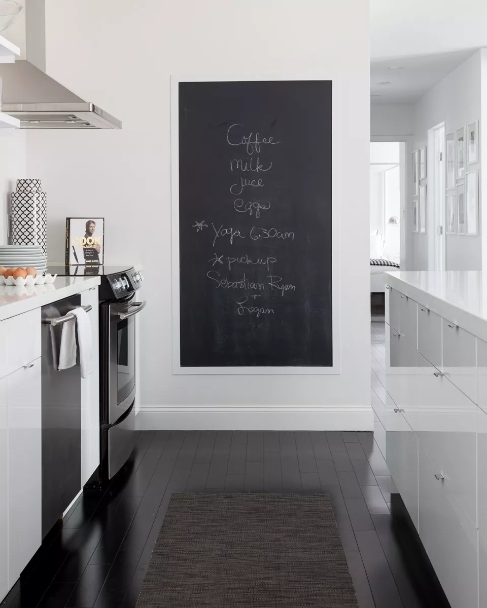 Black-and-white kitchen with large framed chalkboard and practical storage solutions
