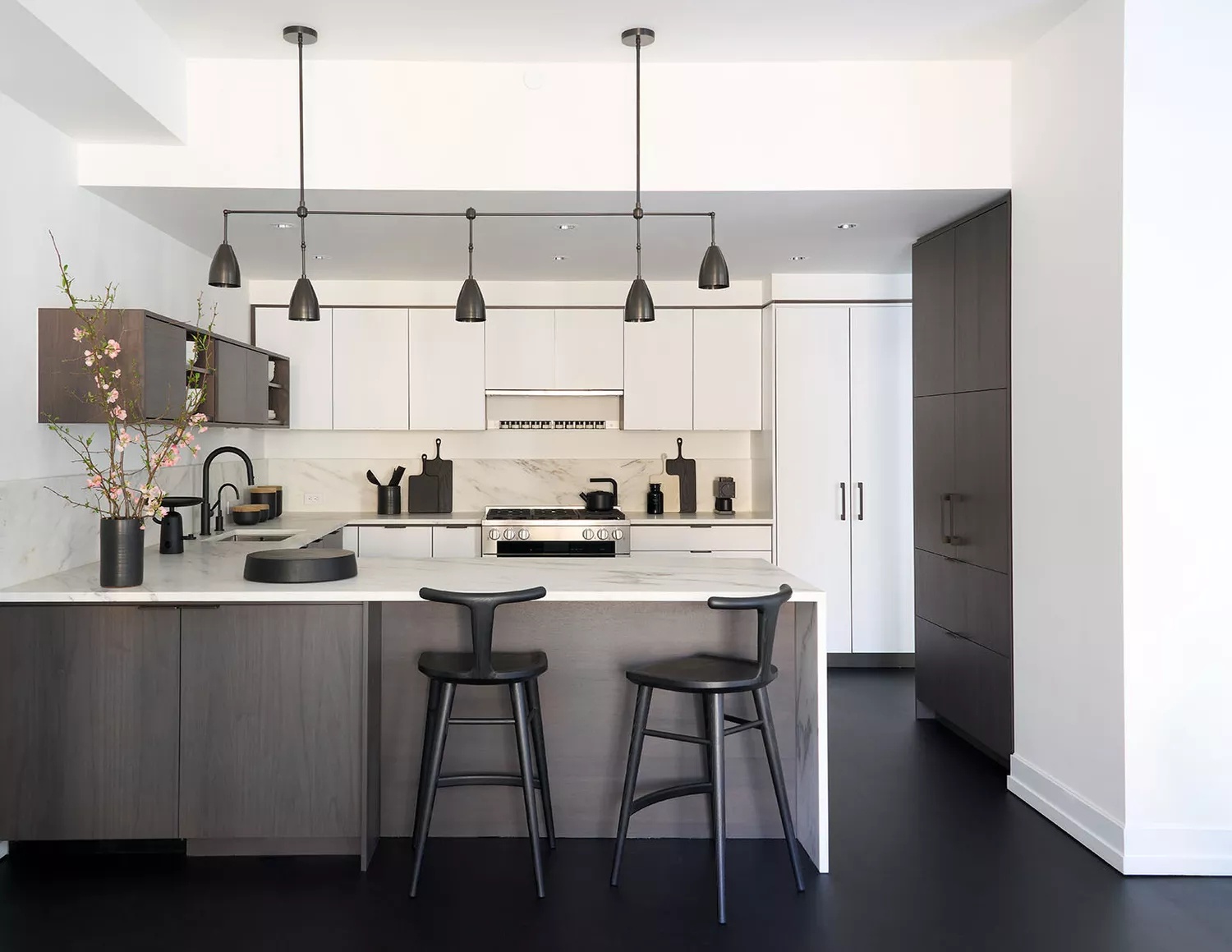 Contemporary black-and-white kitchen with black flooring, large pendant light, sculptural bar stools, and white and dark brown wood cabinetry