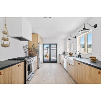 Crisp galley-style kitchen with white walls, black countertops, and warm wood accents