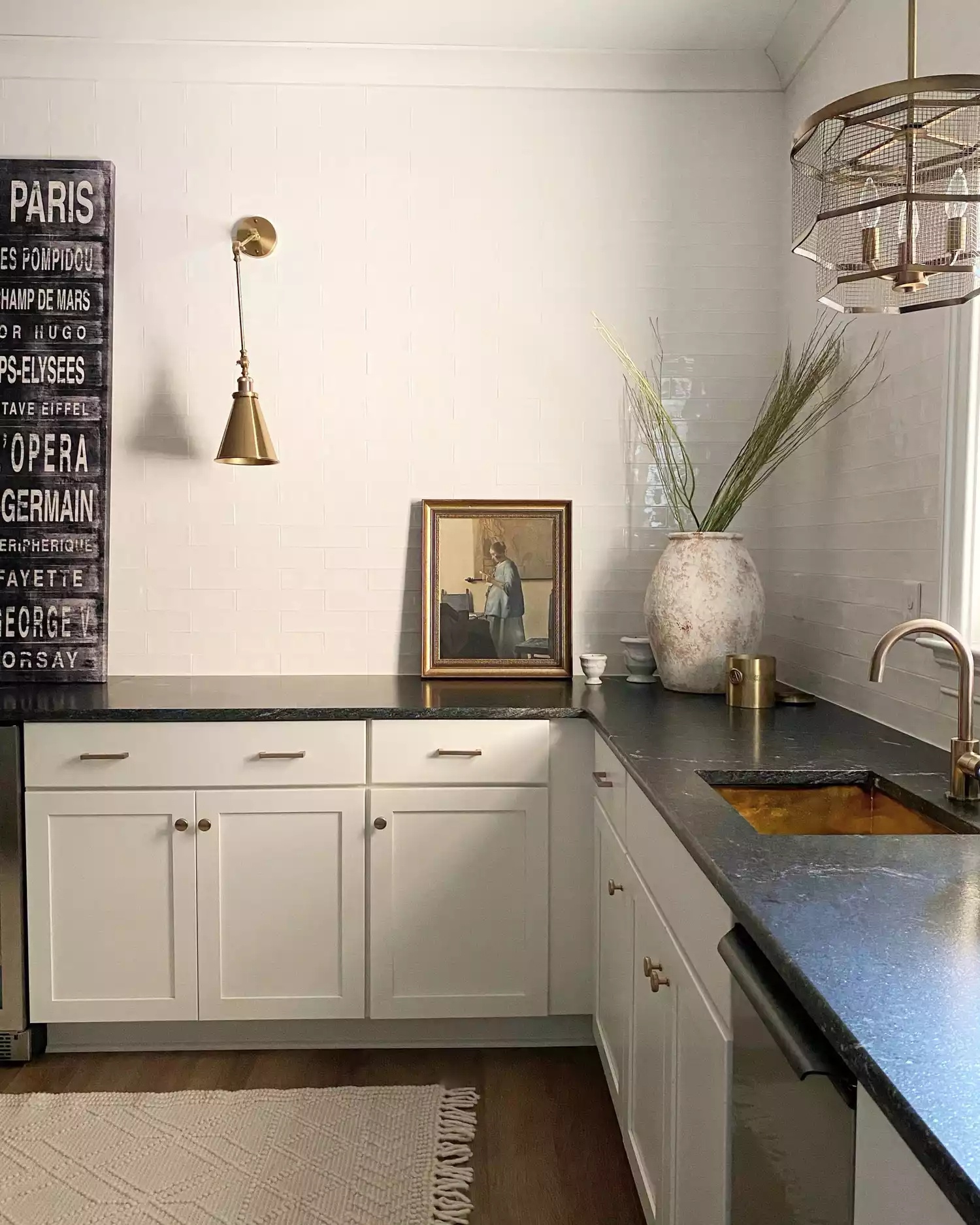 Minimalist black-and-white kitchen with vintage decor accents, glossy white tile walls, black stone countertops, and white cabinets