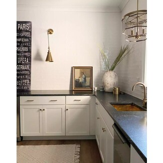 Minimalist black-and-white kitchen with vintage decor accents, glossy white tile walls, black stone countertops, and white cabinets