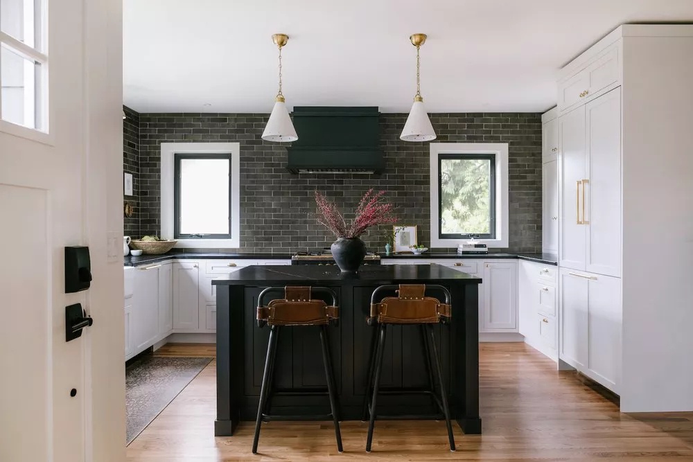 Modern kitchen with pale grayish-black subway tiles, black hood range, white cabinets, and gold details