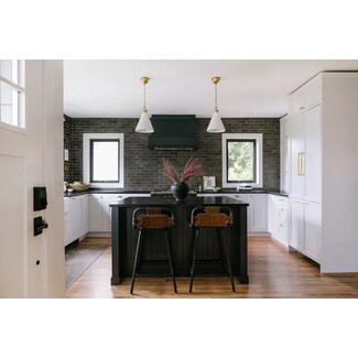 Modern kitchen with pale grayish-black subway tiles, black hood range, white cabinets, and gold details