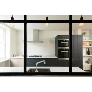Modern minimalist London kitchen with white oak and blackened wood cabinets, industrial metal and glass partition, and stainless steel accents
