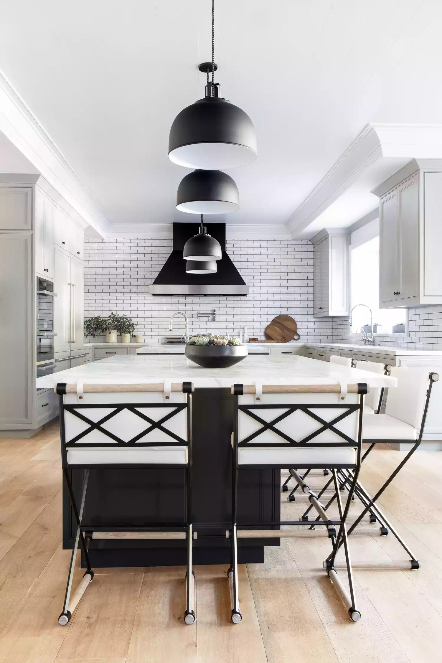 Sprawling kitchen with black pendant lights, white subway tile wall, and black-and-white bar stools