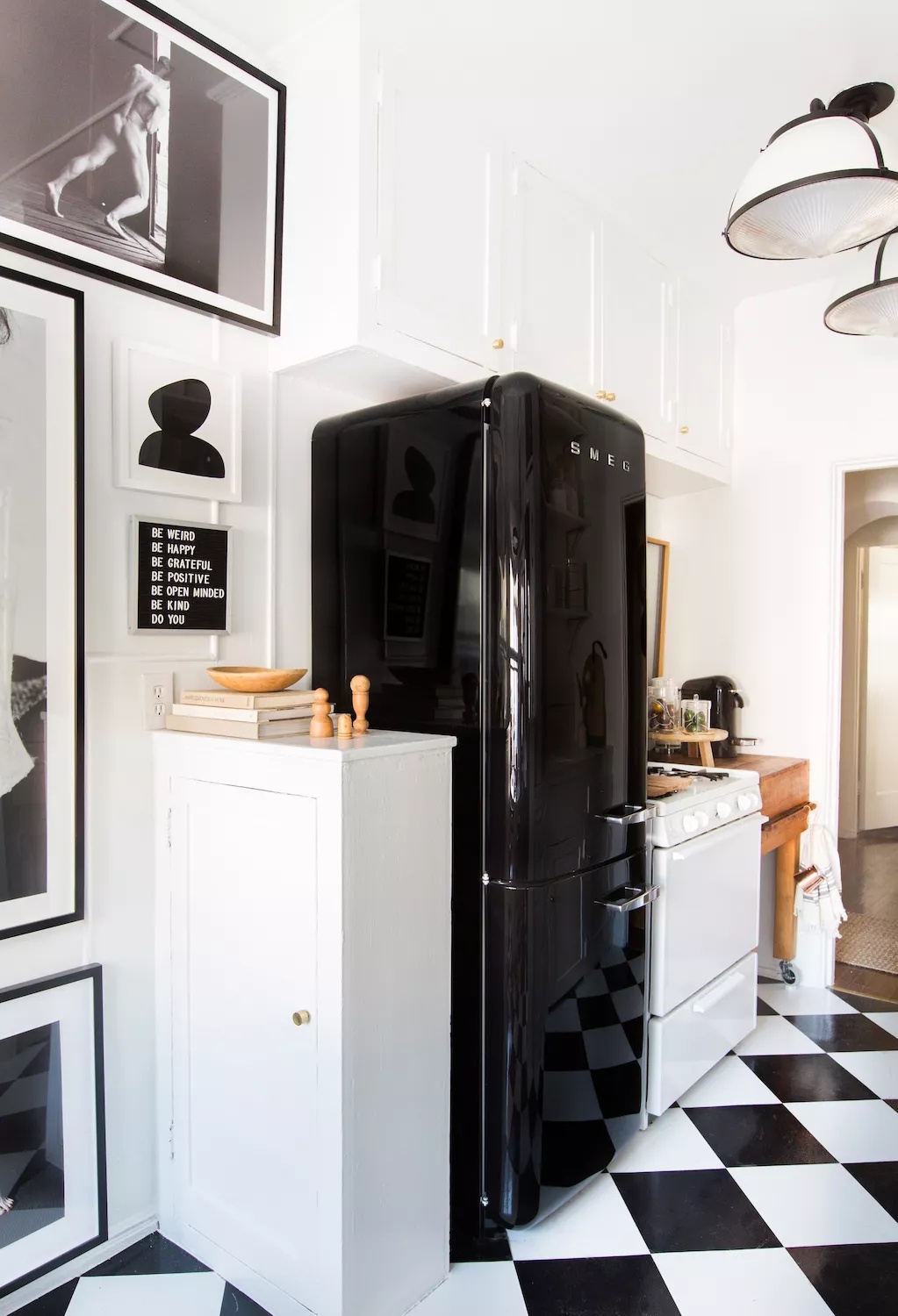 Sunny black-and-white kitchen with black-and-white tile flooring, glossy black vintage-style fridge, and monochrome wall art