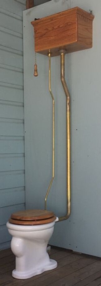 High Tank Toilet featuring Brass Toned Piping and Red Oak Wood Finish